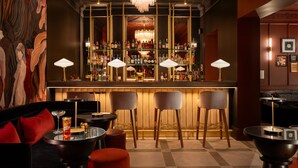 A bar area with a chandelier, multiple bar stools, and a variety of bottles on shelves. - The Green (Dublin)