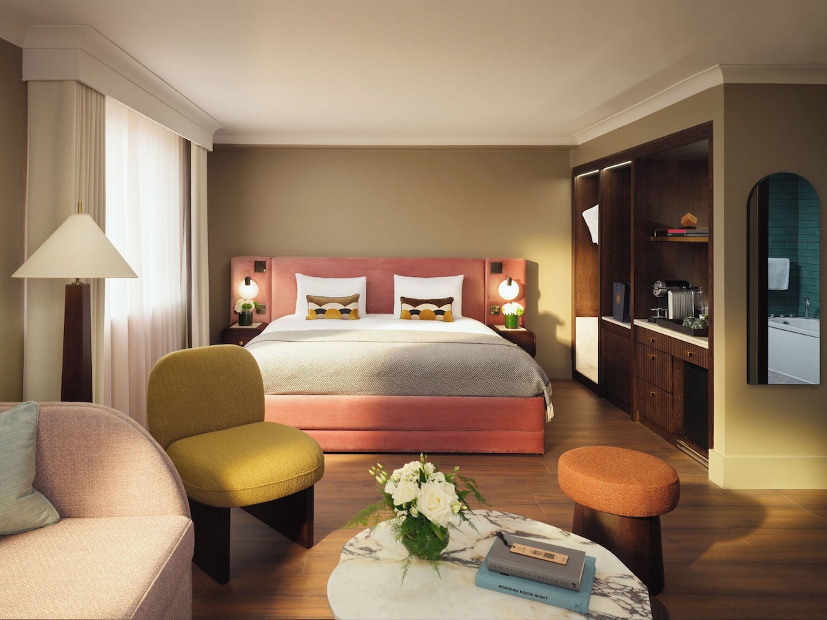 Canopy bed with crisp white pillows and floral-patterned bedding and wallpaper at Hotel Eldorado Paris.