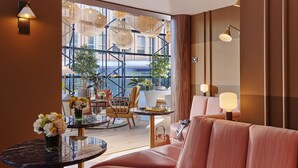 A modern hotel room with a plush pink sofa, a round table with a vase of flowers, and a balcony with outdoor seating and plants. - The Green (Dublin)