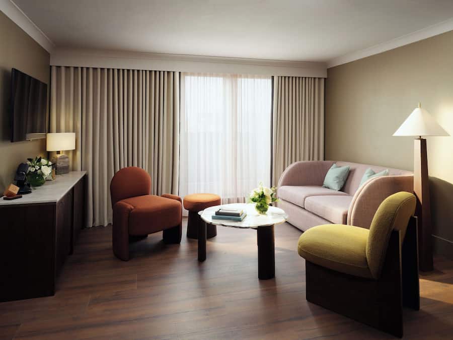 Et hotelværelse med sofa, lænestol, skammel, sofabord, lampe og et skrivebord med telefon og blomster.