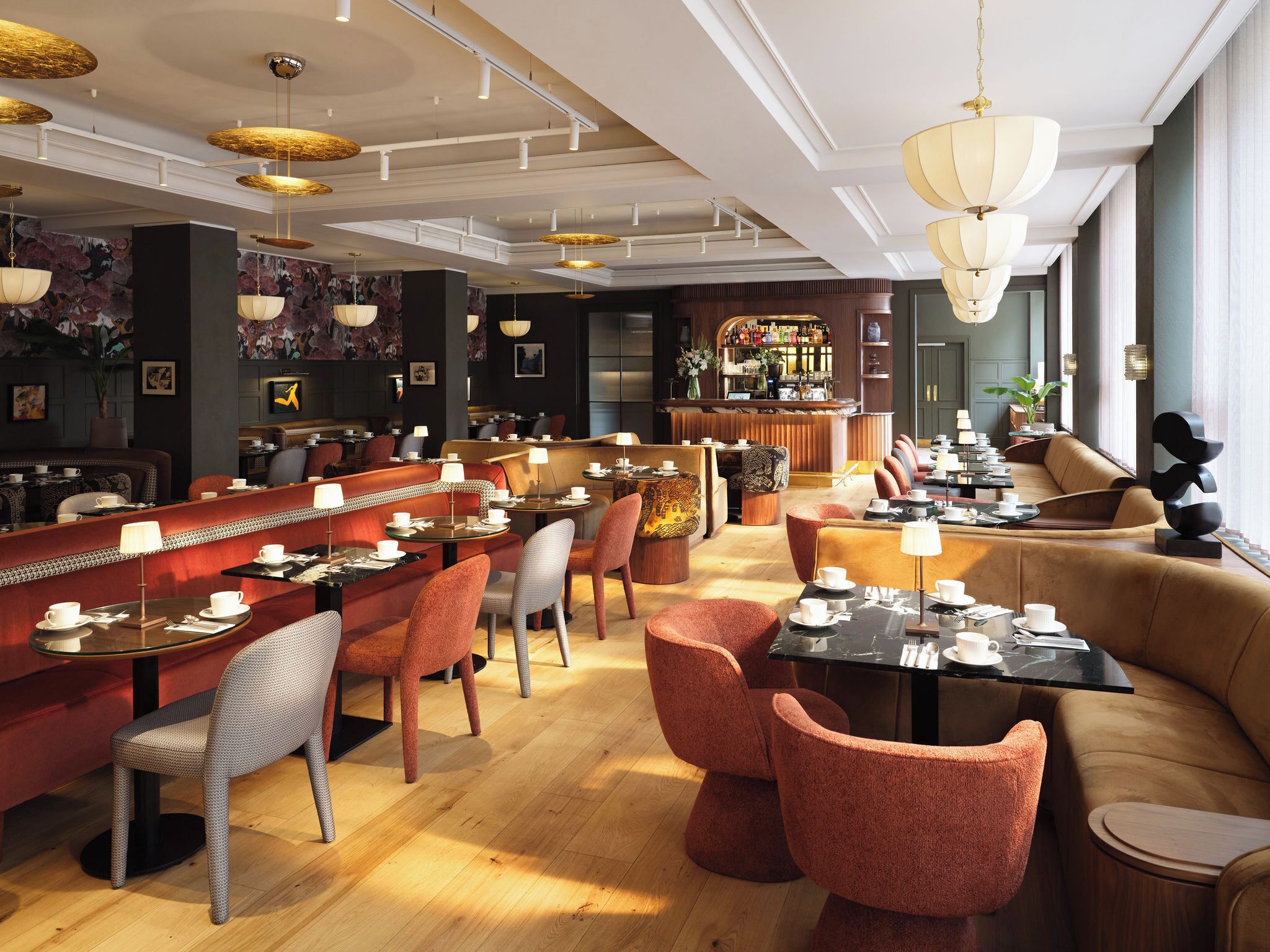 Un restaurant moderne doté d’un bar, de planchers en bois et de différents types de sièges, notamment des banquettes et des tables.
