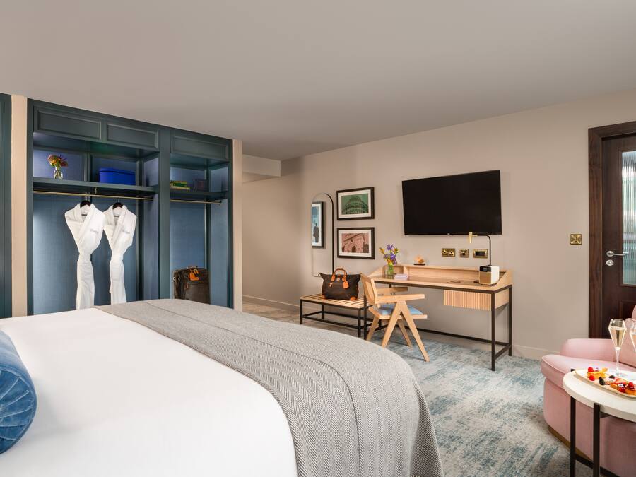 A hotel room with a bed, a desk, a chair, a TV, and a wardrobe.