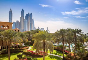 A hotel courtyard with palm trees, a swimming pool, and a city skyline in the background. - One&Only Royal Mirage (Dubai)