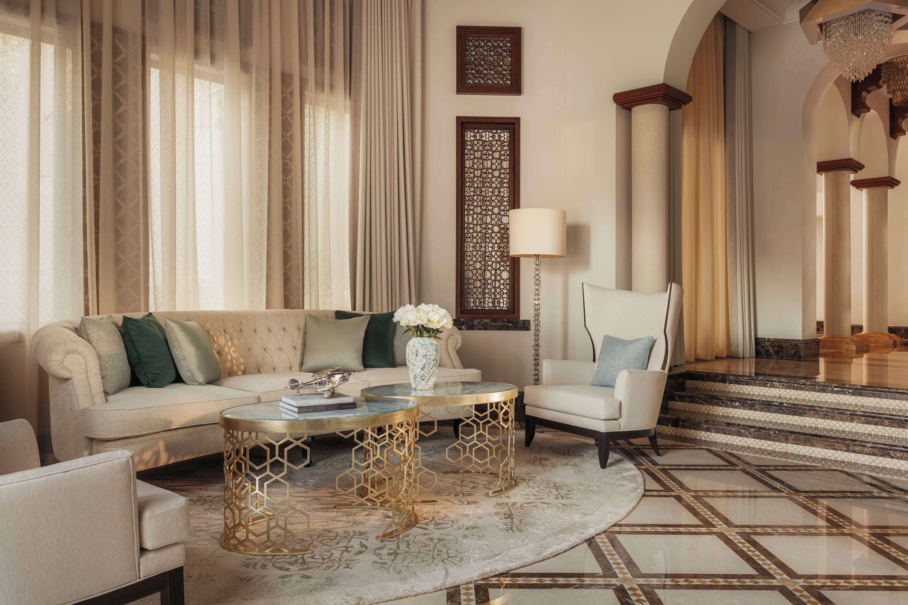 A luxurious living room with a beige sofa, a round coffee table, and a white armchair. There is a decorative vase with flowers on the coffee table.