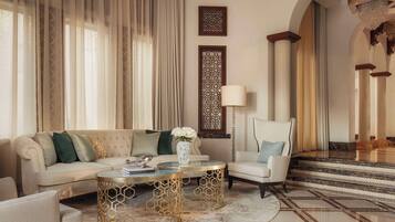 A luxurious living room with a beige sofa, a round coffee table, and a white armchair. There is a decorative vase with flowers on the coffee table.