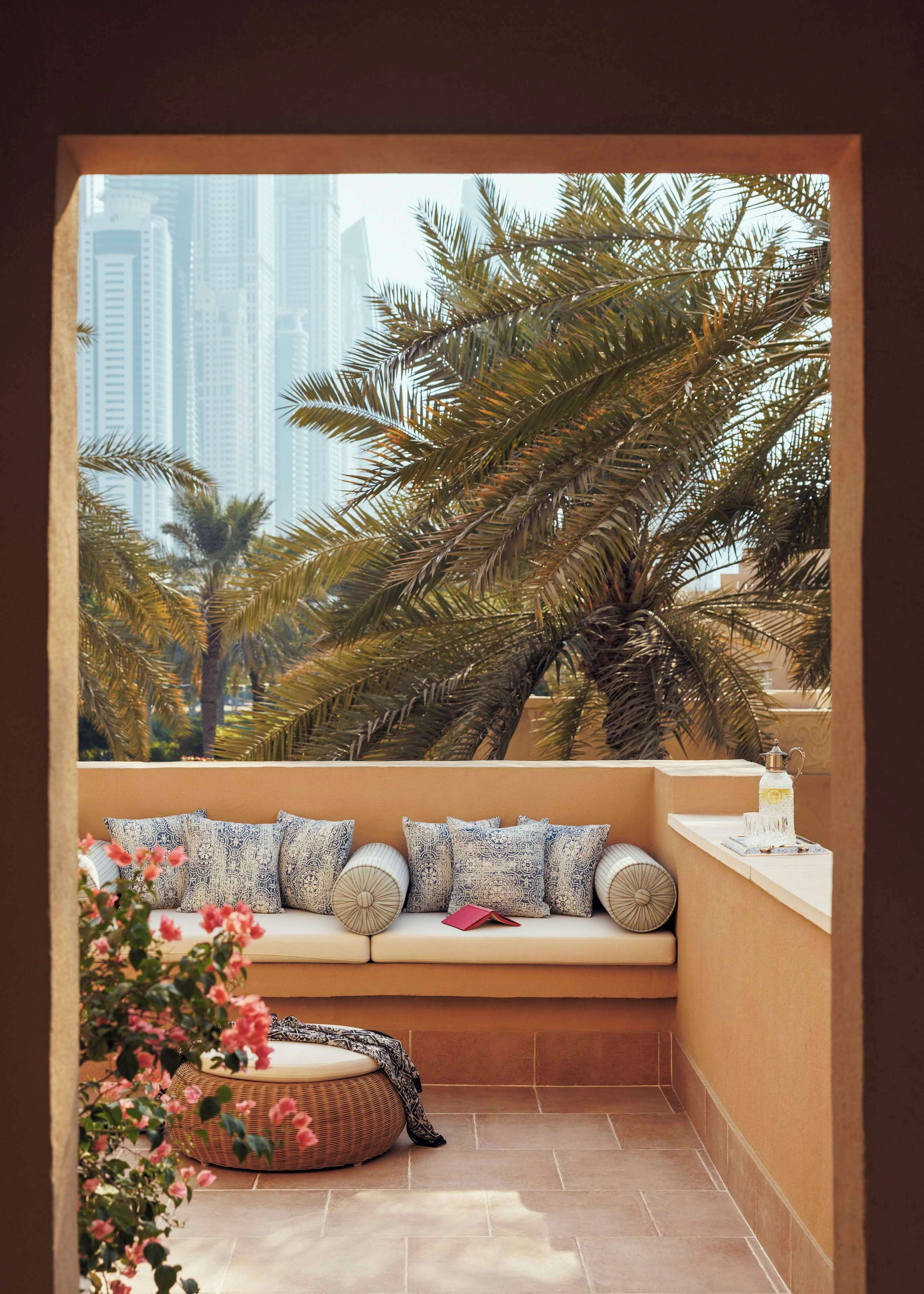 Een balkon met een zachte zithoek, een rieten poef en een decoratief item op de vensterbank.
