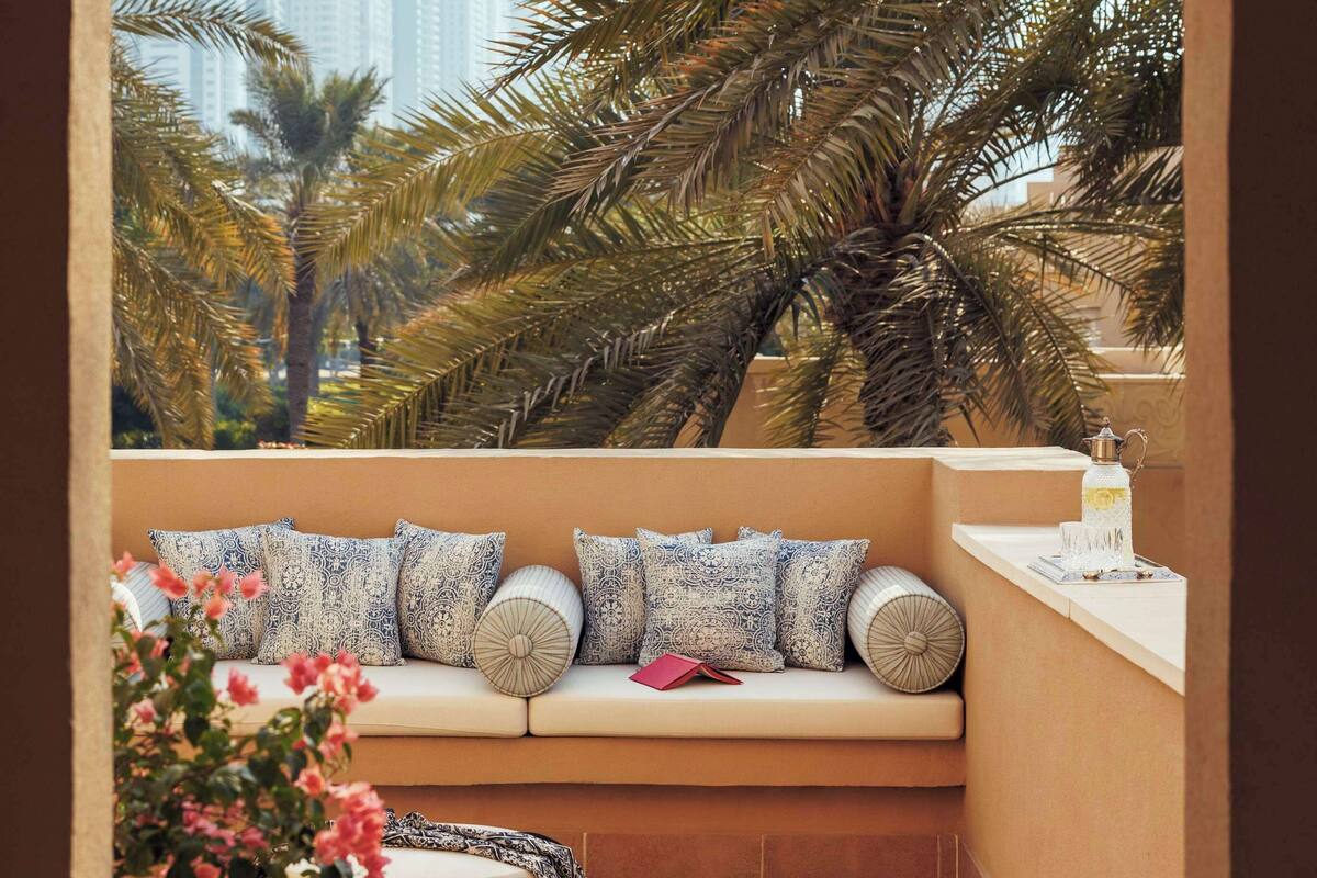 Ein Balkon mit einer Sitzgruppe mit Auflagen, einem Korpus-Pouff und einem dekorativen Gegenstand auf der Fensterbank.