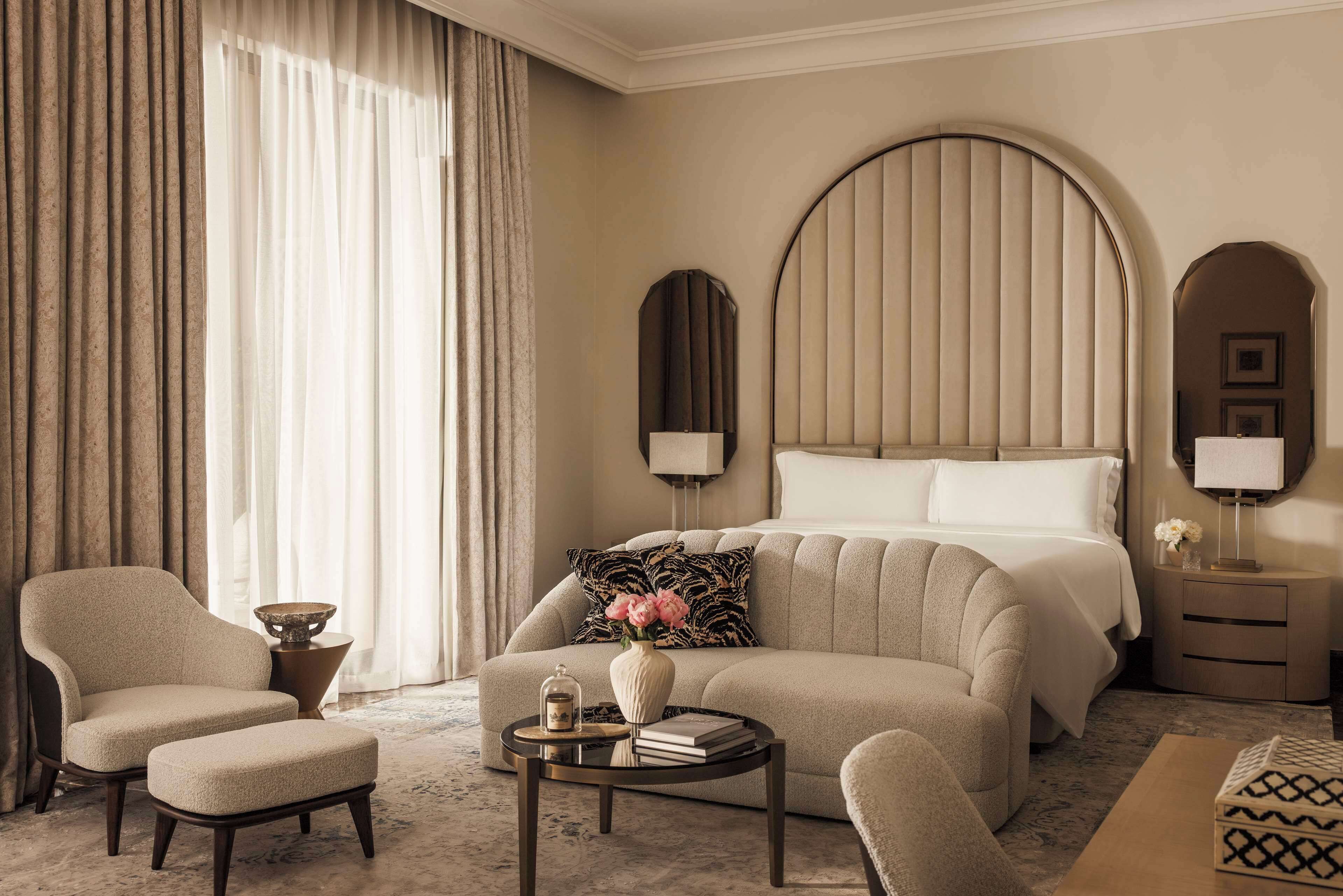 A hotel room with a large bed, two armchairs, a small table with a vase and books, and a nightstand with lamps.
