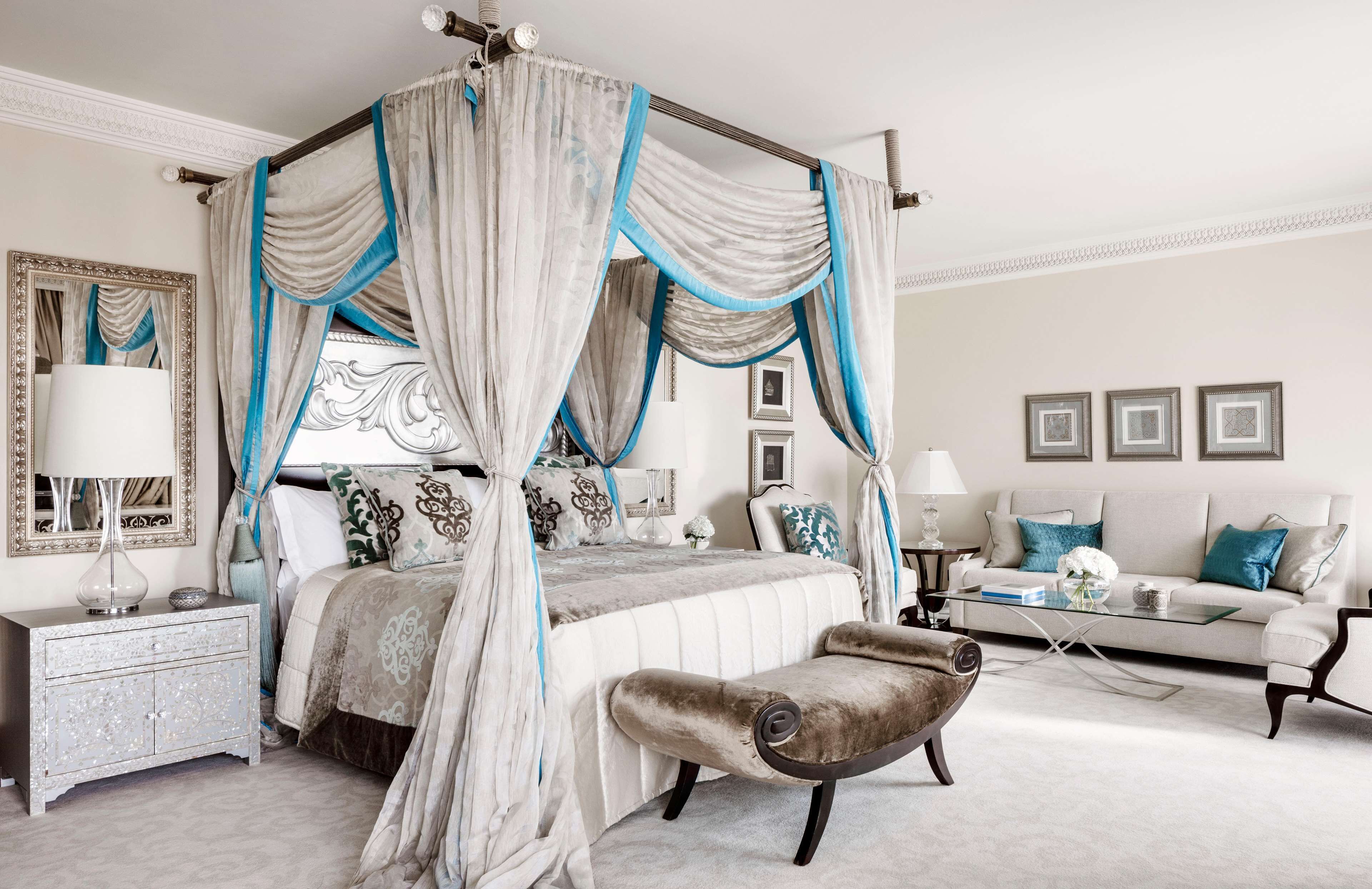 Een hemelbed met nachtkastje, een chaise longue, een bank en ingelijste foto's aan de muur.