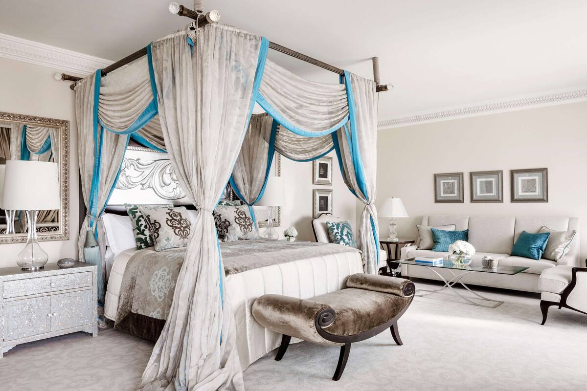 Ein Bett mit Himmelbett, ein Nachttisch, eine Chaise longue, eine Couch und gerahmte Bilder an der Wand.