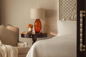 Quarto de hotel com uma cama, uma mesa de cabeceira com luminária, um vaso com flores e um painel decorativo na parede.