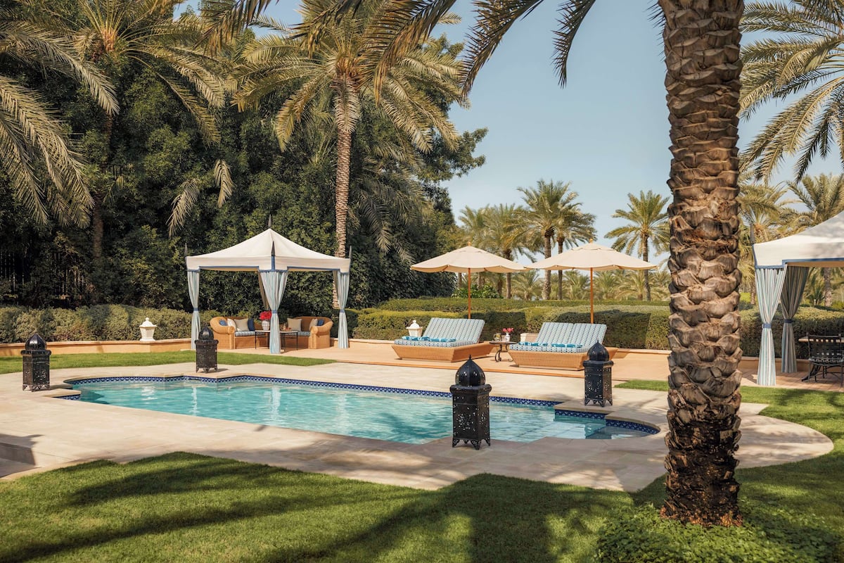 Ein Poolbereich mit Liegestühlen und Sonnenschirmen, umgeben von Palmen und einer Laube.