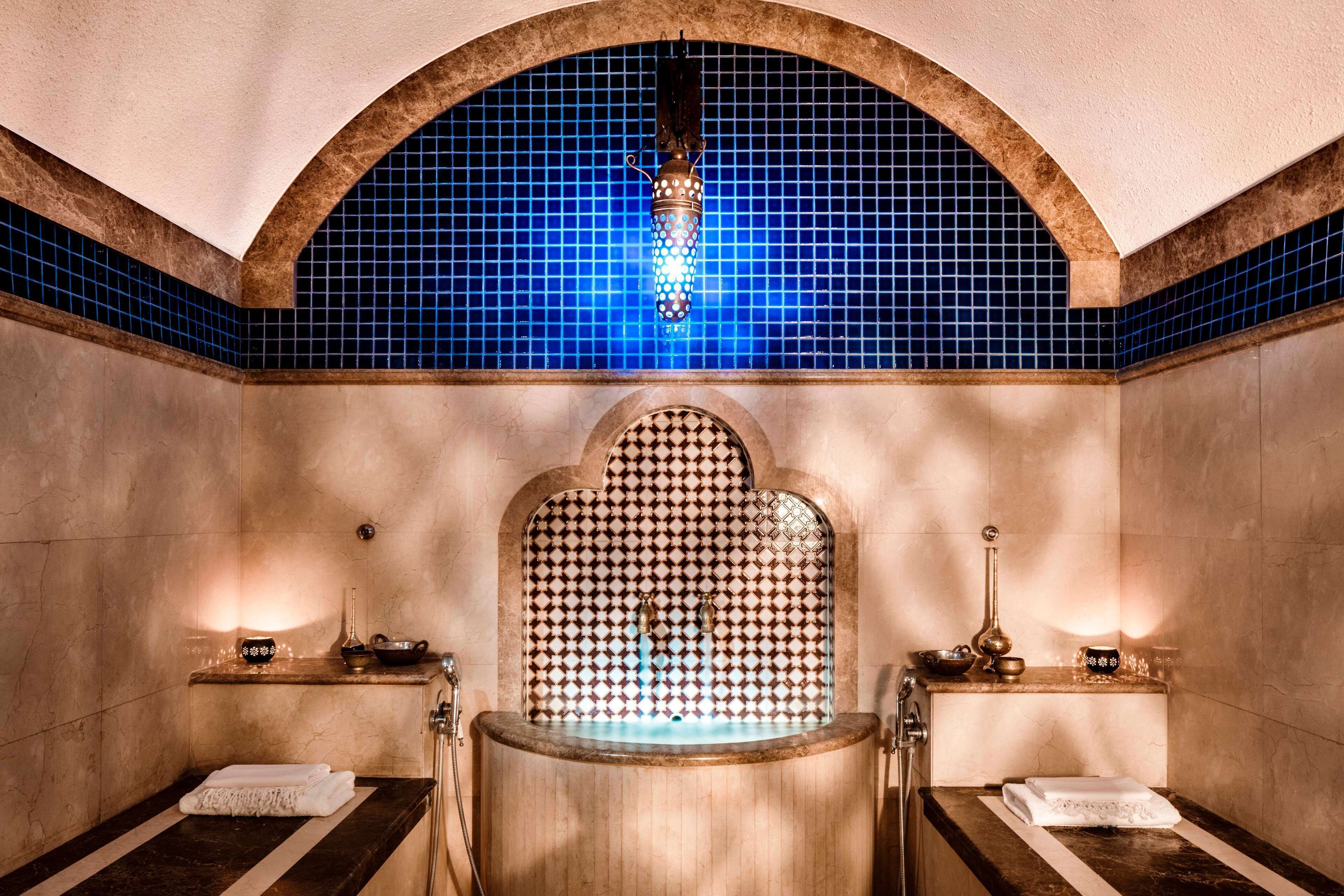 A spa room with a large bathtub, a blue-tiled wall, and a decorative arch above the tub.