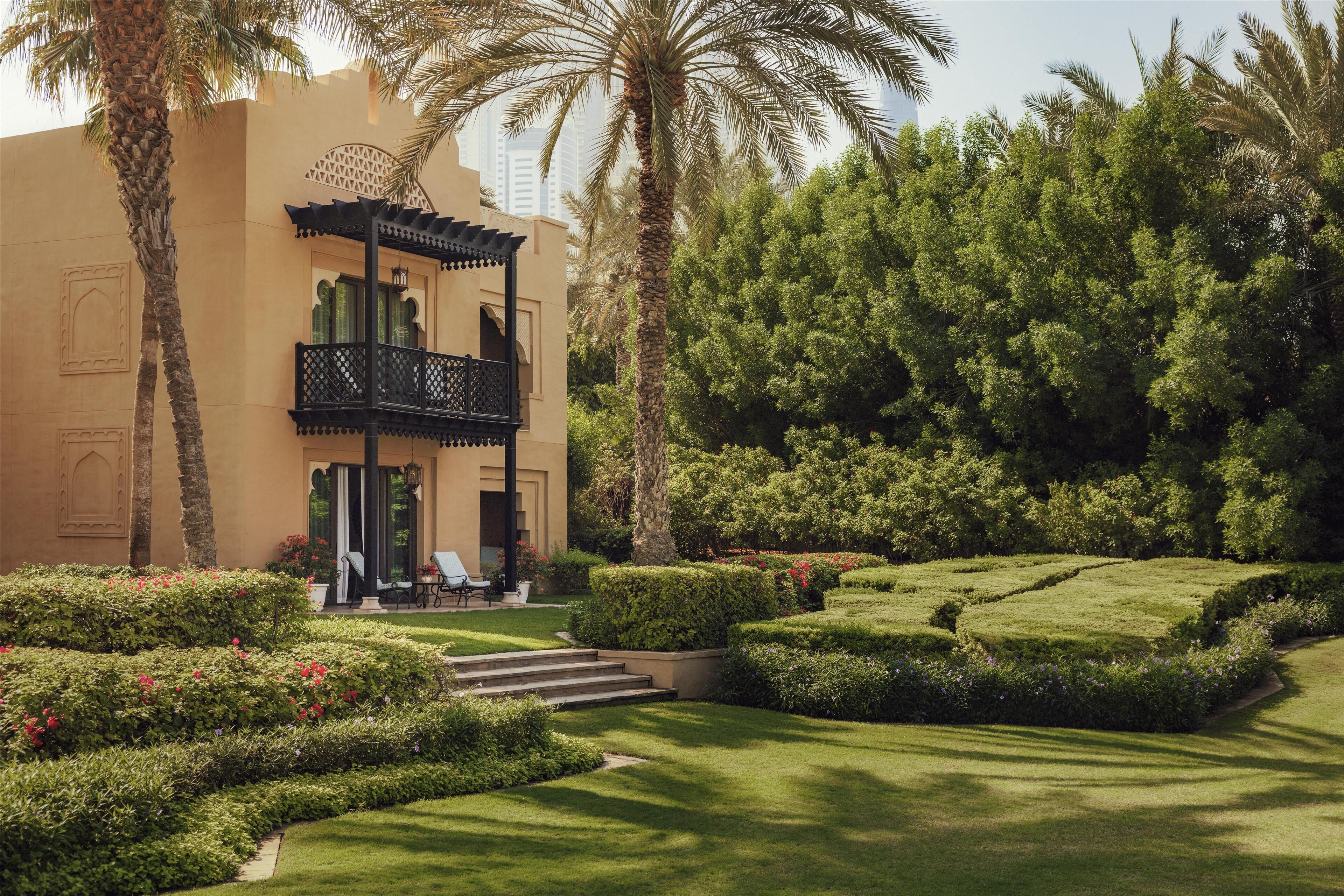 A building with a balcony, surrounded by well-manicured gardens and palm trees.
