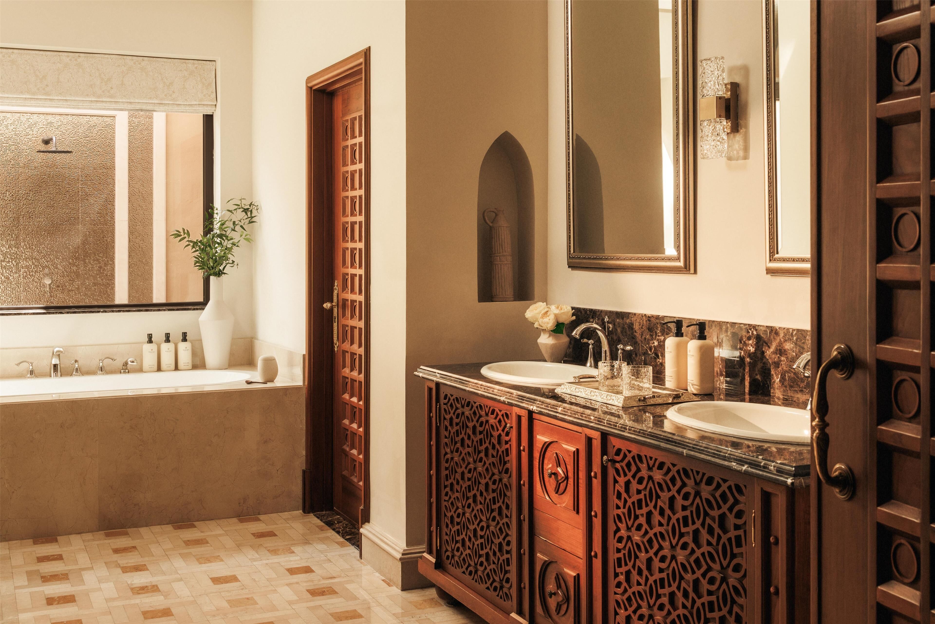 A bathroom with a large mirror, two sinks, a bathtub, and a decorative cabinet.