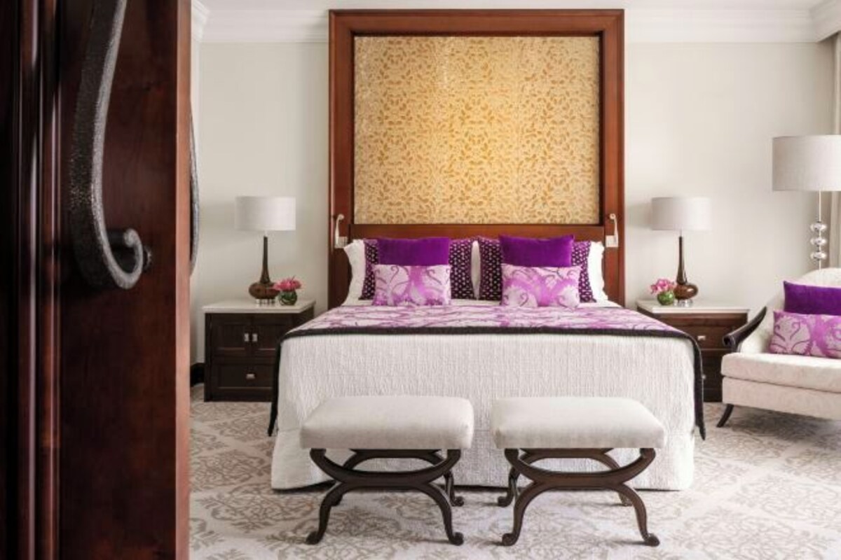 A bedroom with a large bed, two bedside tables, a nightstand, a chair, and a decorative headboard.