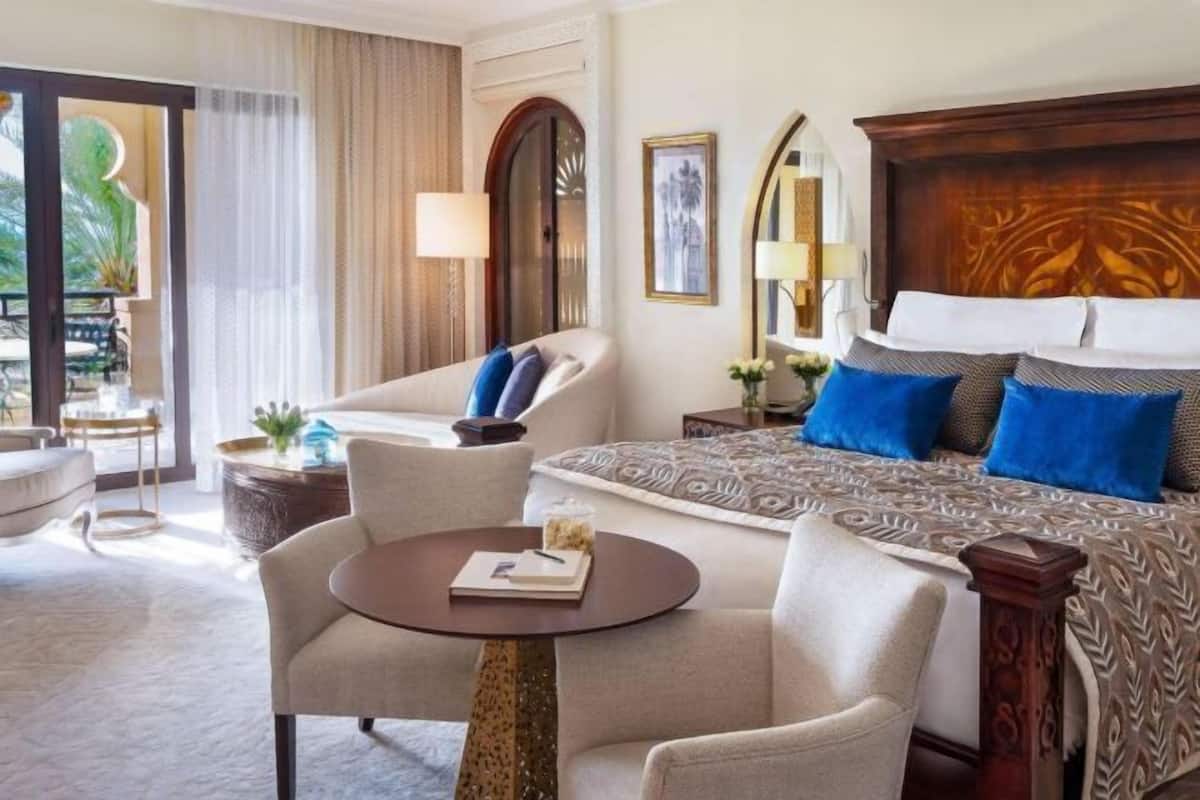 A hotel room with a bed, two armchairs, a small round table, and a view of the outdoors.