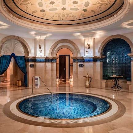A luxurious indoor swimming pool with a circular design, surrounded by elegant arches and a tiled floor.