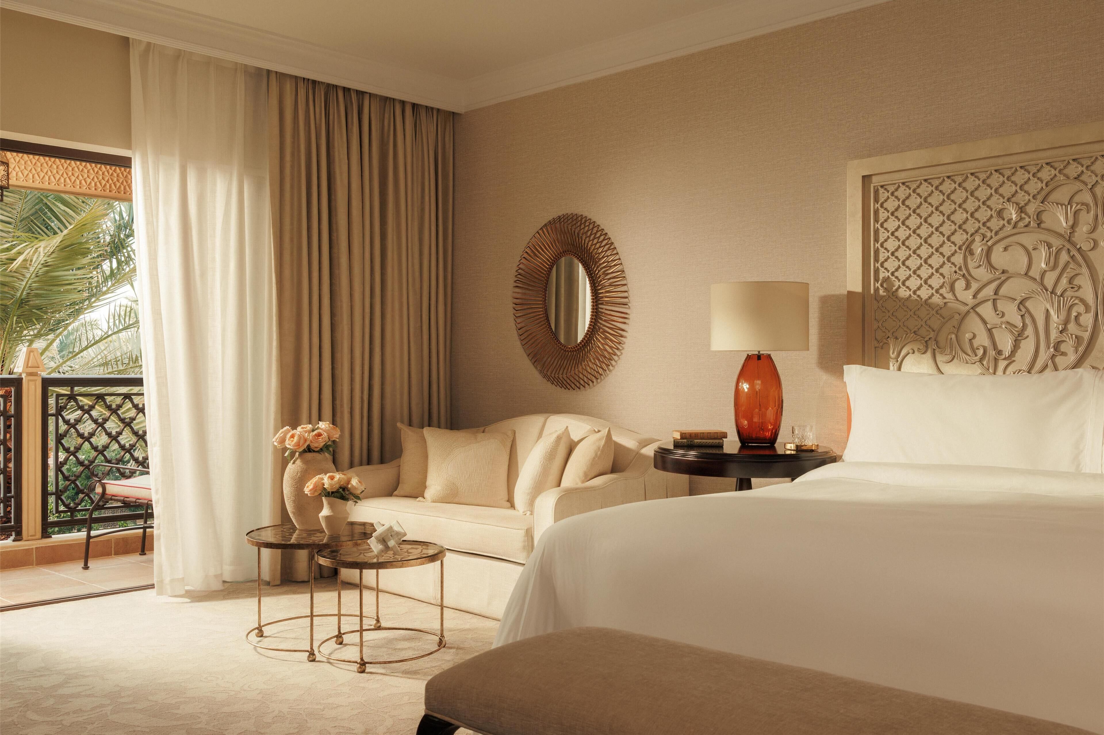 Hotelkamer met een bed, een slaapbank, een klein tafeltje met een bloevas, een ronde spiegel en een decoratief wandpaneel.