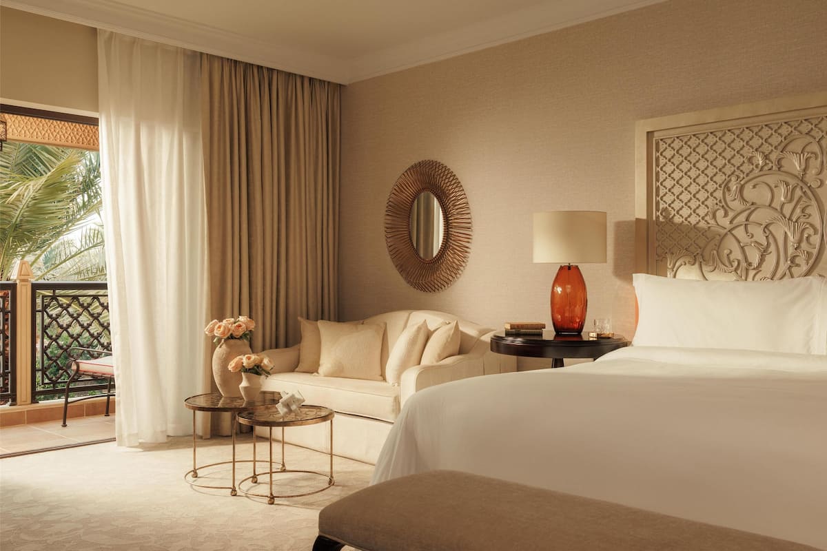 Ein Hotelzimmer mit einem Bett, einer Couch, einem kleinen Tisch mit Blumenvase, einem runden Spiegel und einer Wandverkleidung.