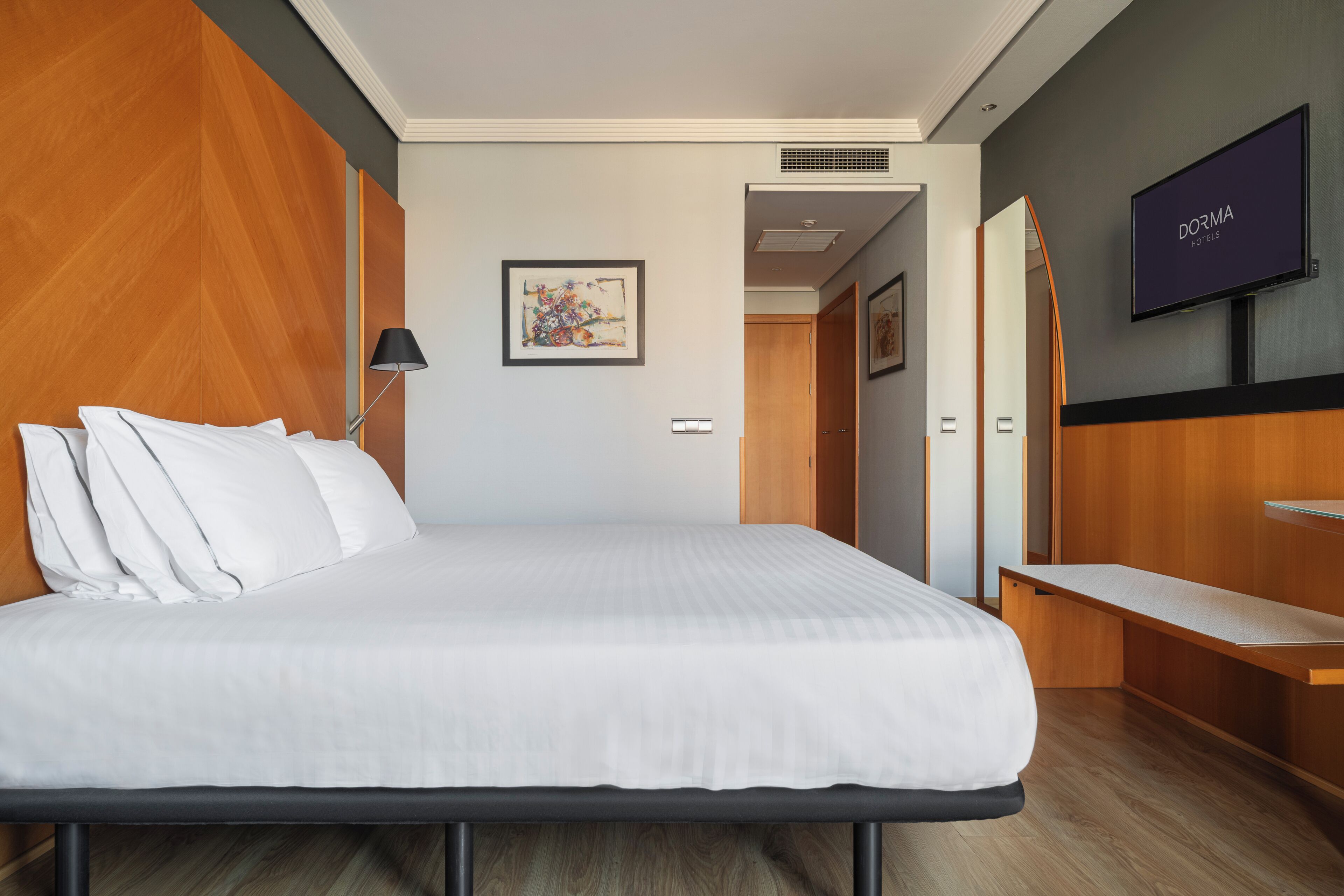 Una habitación de hotel moderna con una cama grande, un escritorio, un televisor y un cuadro en la pared.