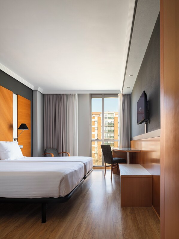 Habitación de hotel con cama, escritorio, silla, televisión y ventana con vistas a edificios.