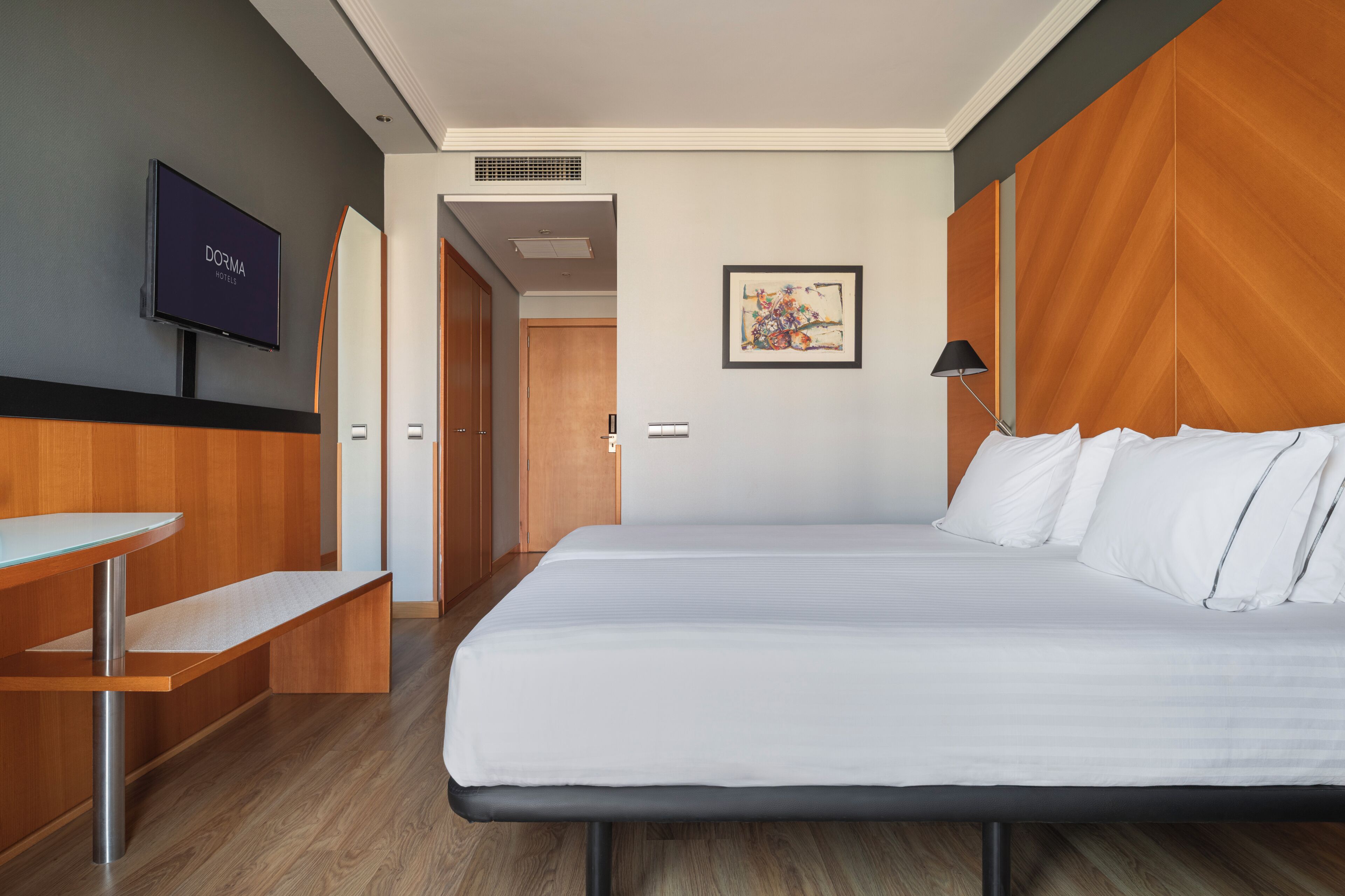Une chambre d’hôtel avec un lit, une télévision, un bureau et un tableau au mur.