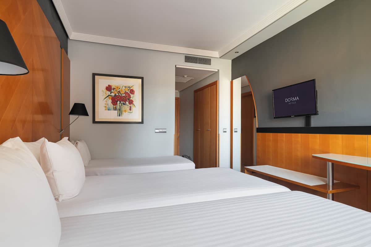 A hotel room with two beds, a desk, a television, and a framed picture on the wall.