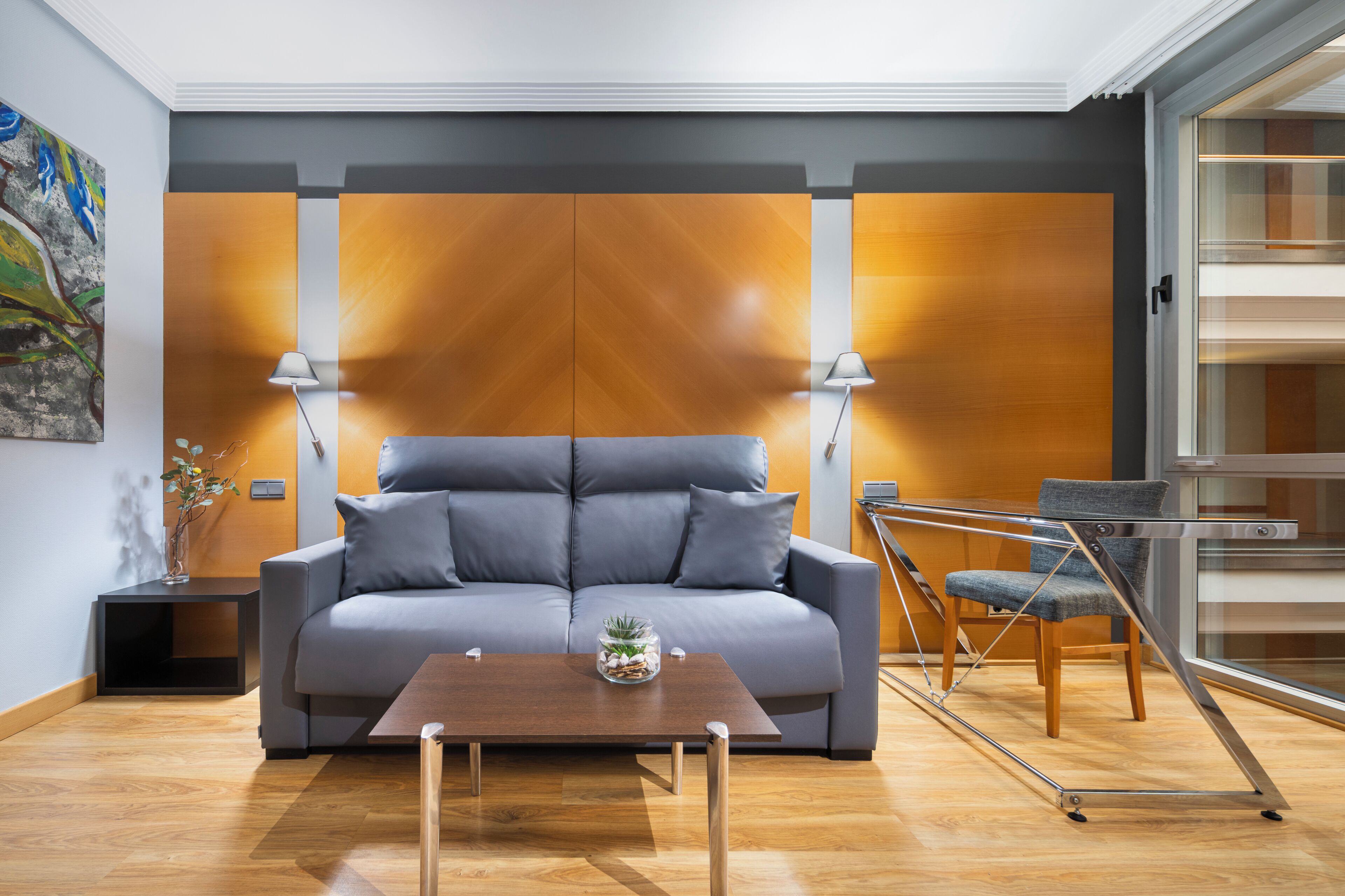 Una sala de estar moderna con un sofá gris, una mesa de centro de madera y un ventanal que da a un balcón.
