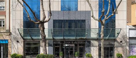 A hotel entrance with a glass facade, potted plants, and a bench.