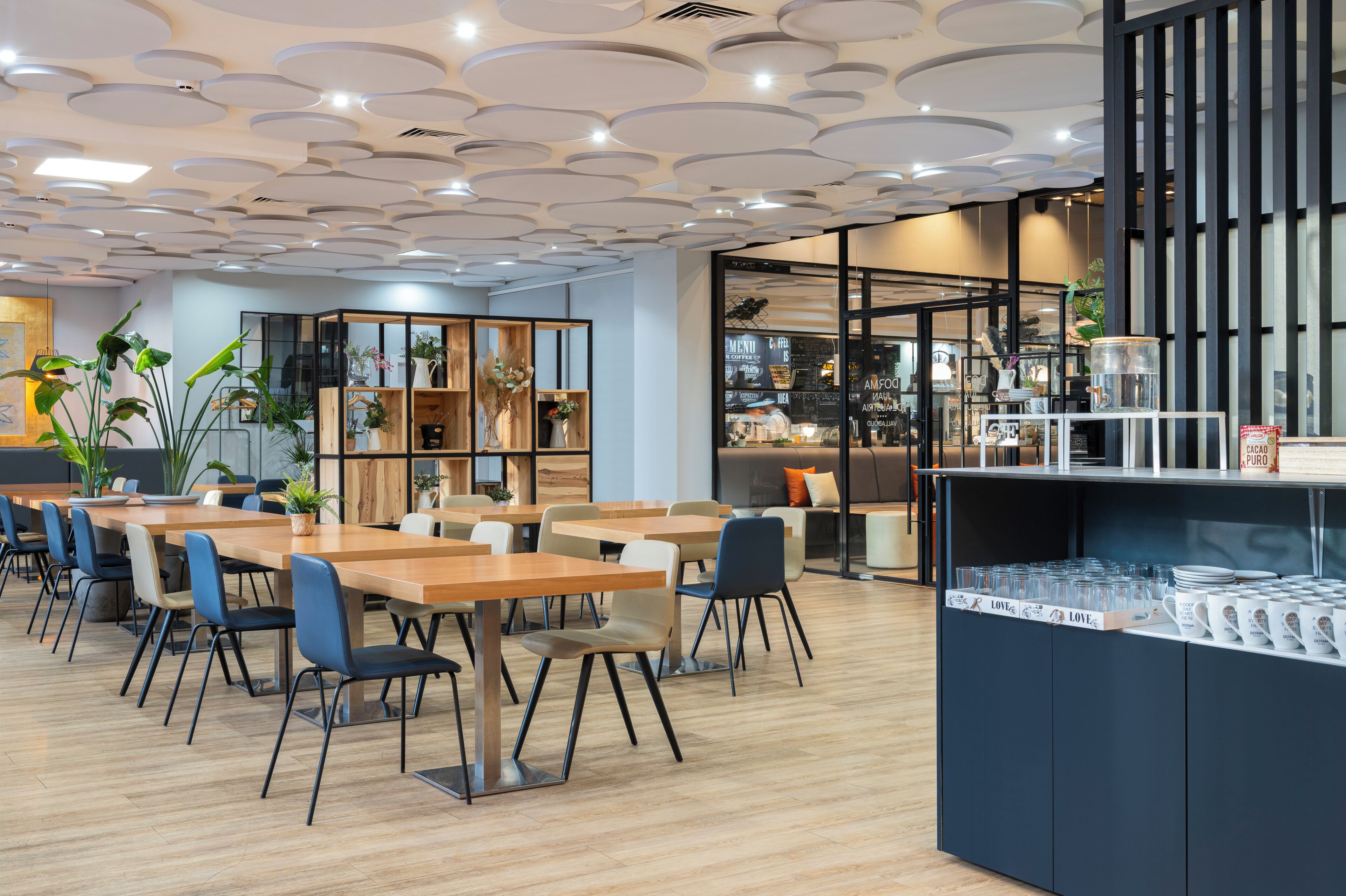 A modern cafe with wooden tables and chairs, a coffee bar, and a variety of plants.