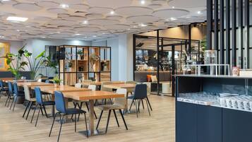 A modern cafe with wooden tables and chairs, a coffee bar, and a variety of plants.