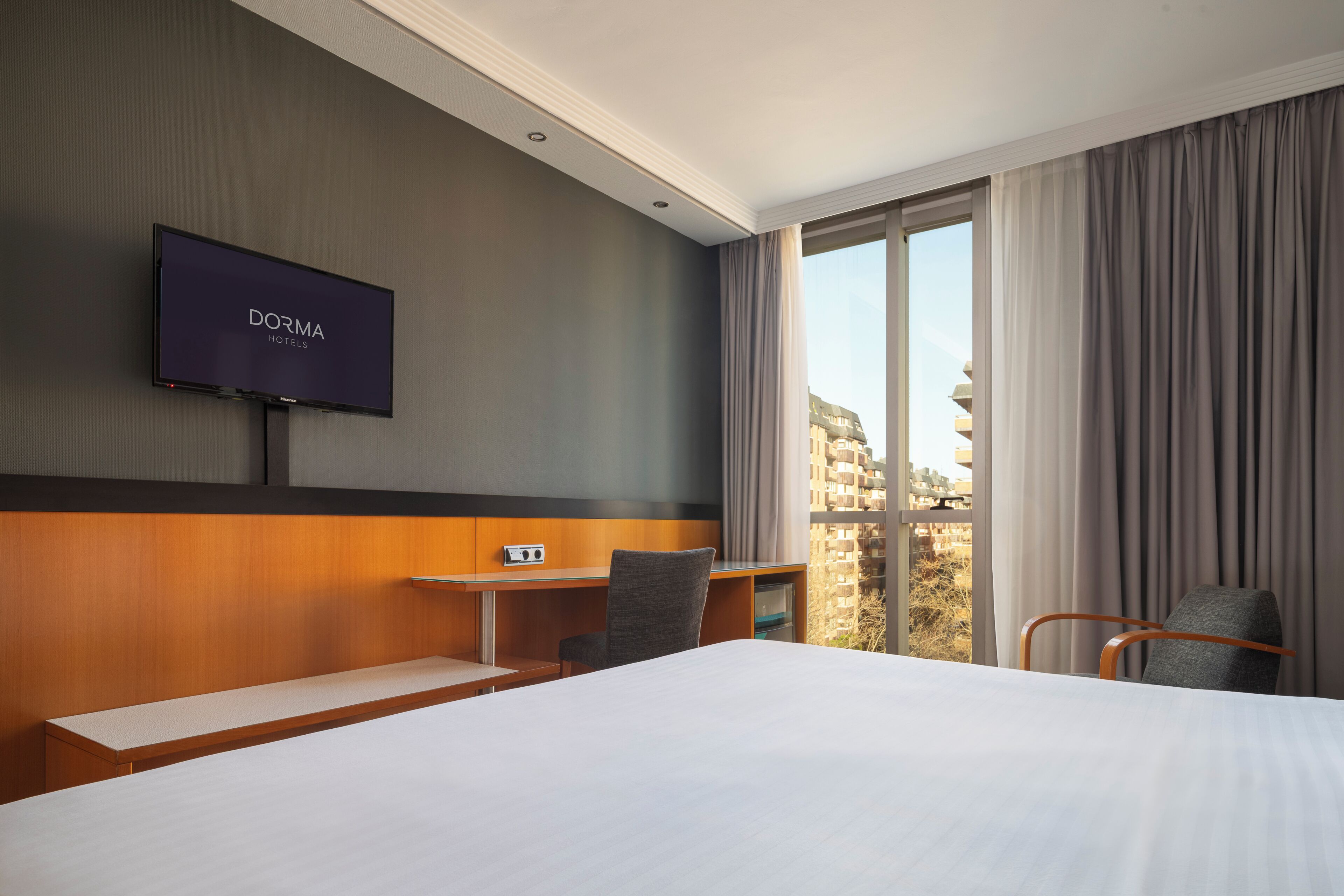 A hotel room with a bed, a desk, a chair, a TV, and a window with curtains.