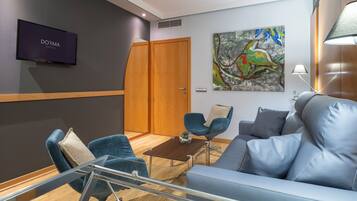 Una habitación de hotel moderna con televisor de pantalla plana, un sofá, dos sillones, una mesa de centro y un cuadro en la pared.