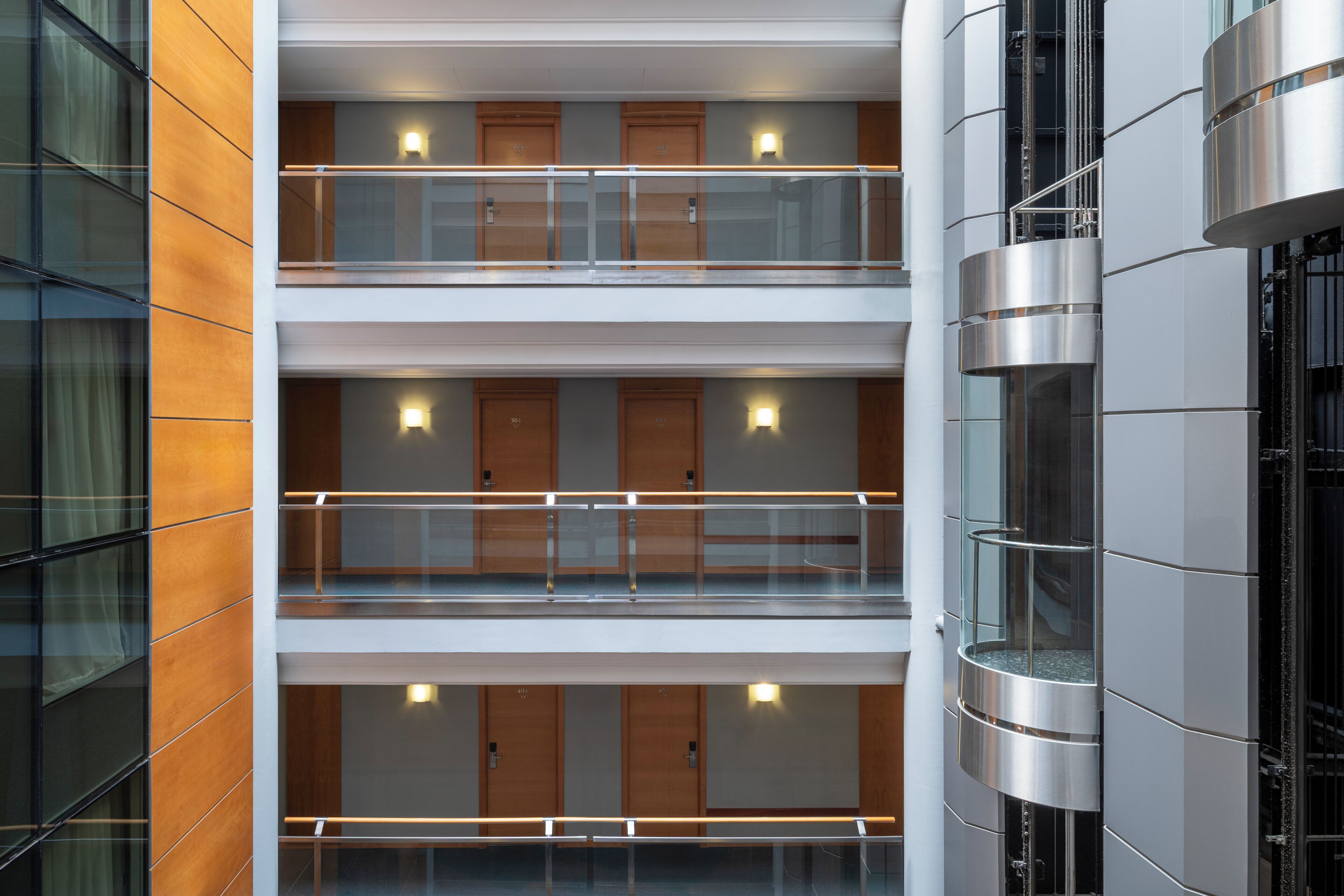 A multi-level hotel interior with glass railings, wooden doors, and a modern design.