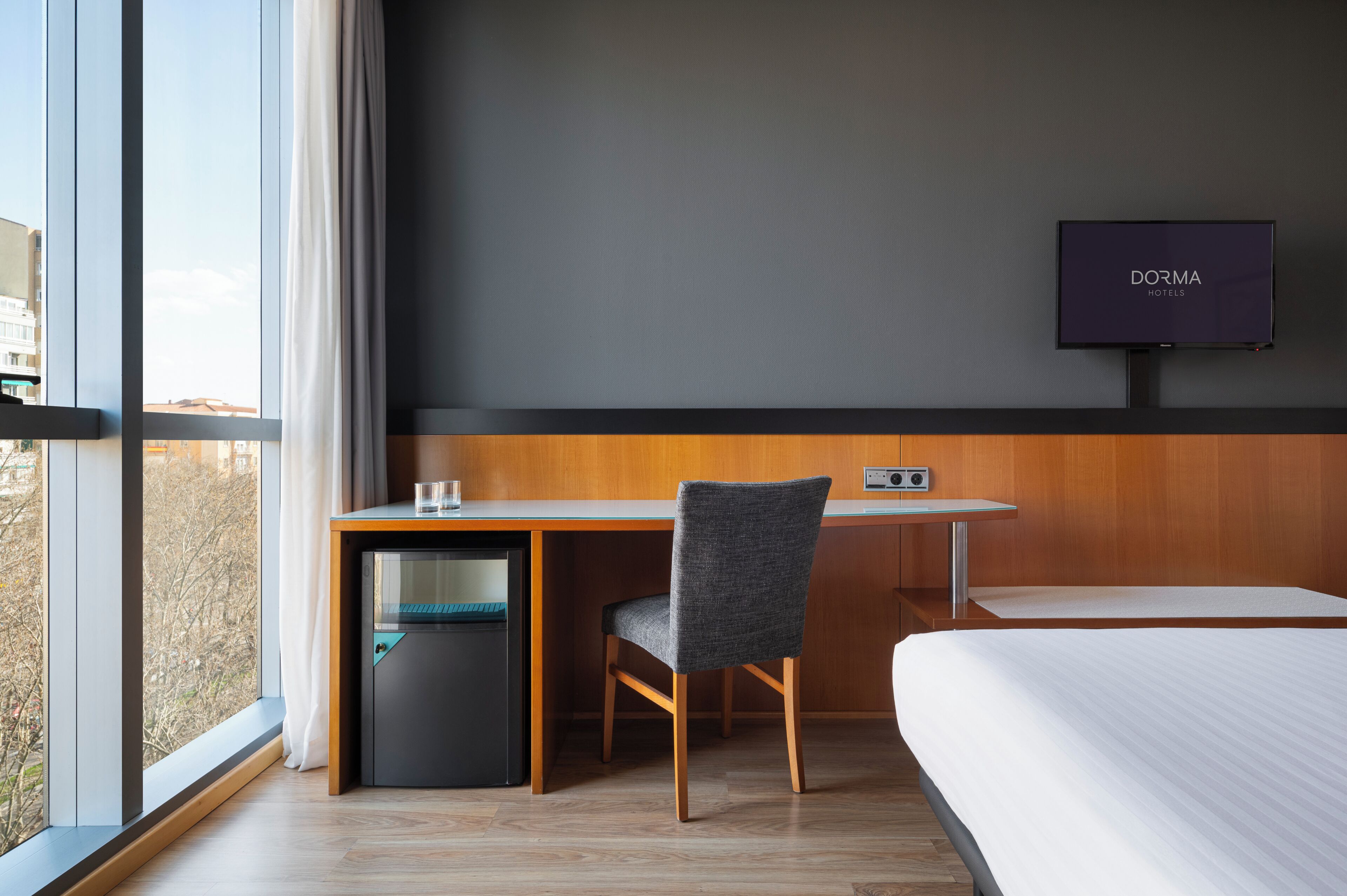 Una habitación de hotel con cama, escritorio con silla, televisor y un refrigerador pequeño.