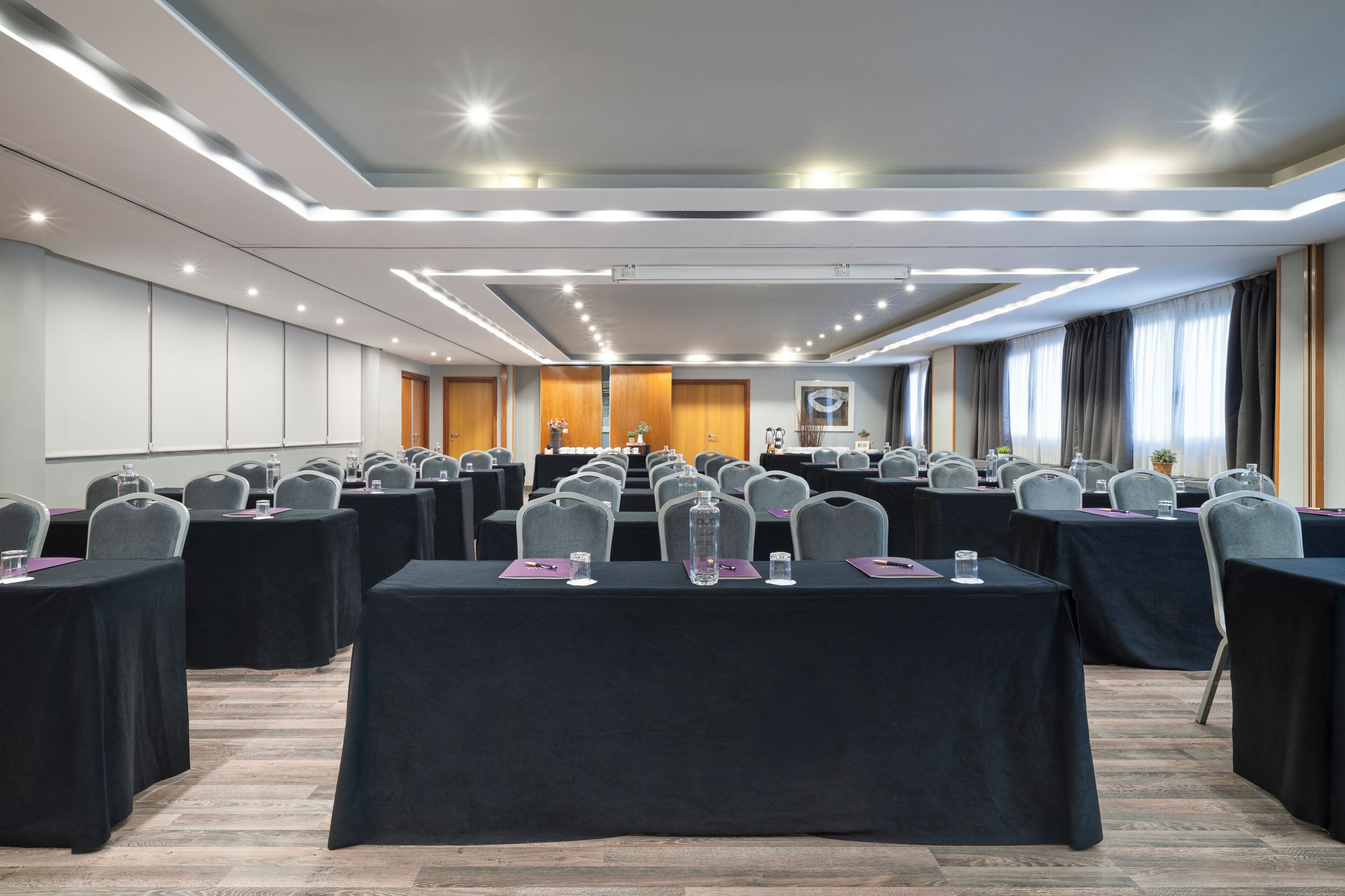 A conference room with rows of tables, chairs, and a ceiling with recessed lighting.