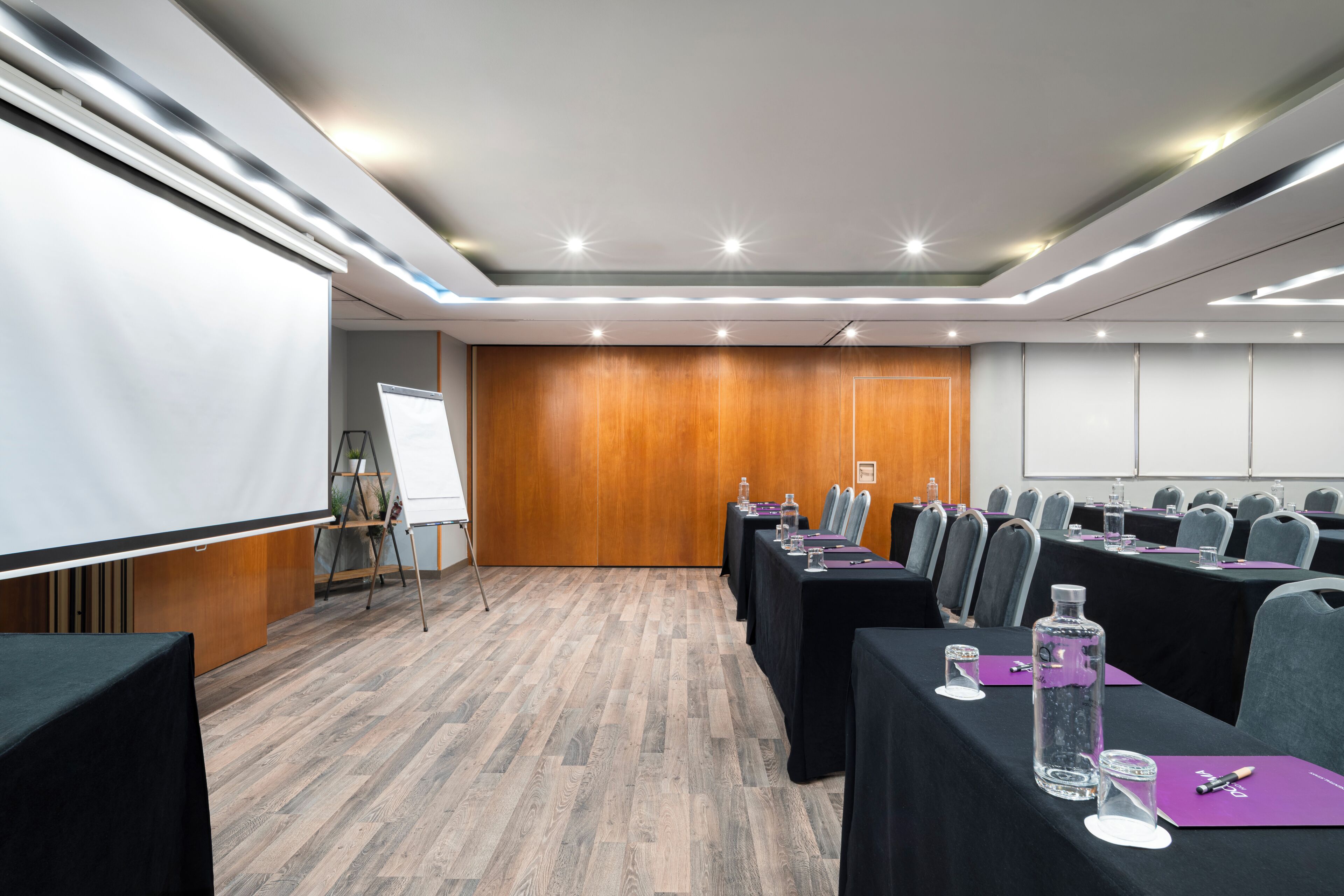 Una sala de conferencias con una pizarra, proyector y filas de mesas con sillas.