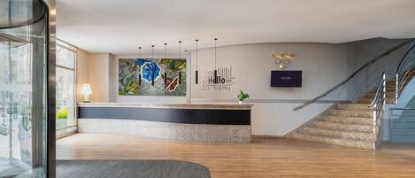 Un espace d’accueil moderne avec un comptoir d’accueil incurvé, une grande peinture abstraite, un panneau indiquant « Bonjour » et un escalier.