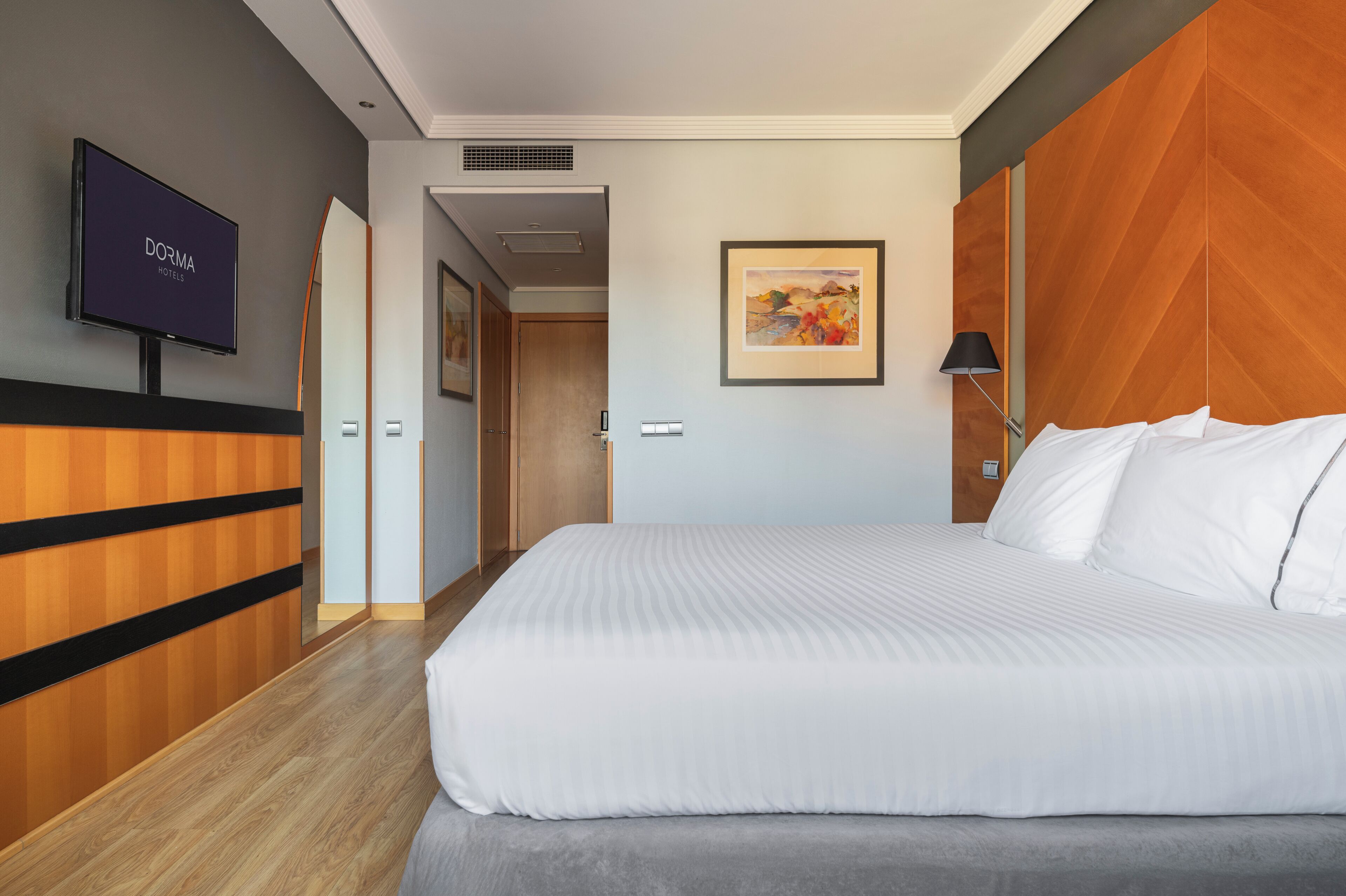 Una habitación de hotel con una cama grande, televisión, un cuadro y una pared de acento de madera.