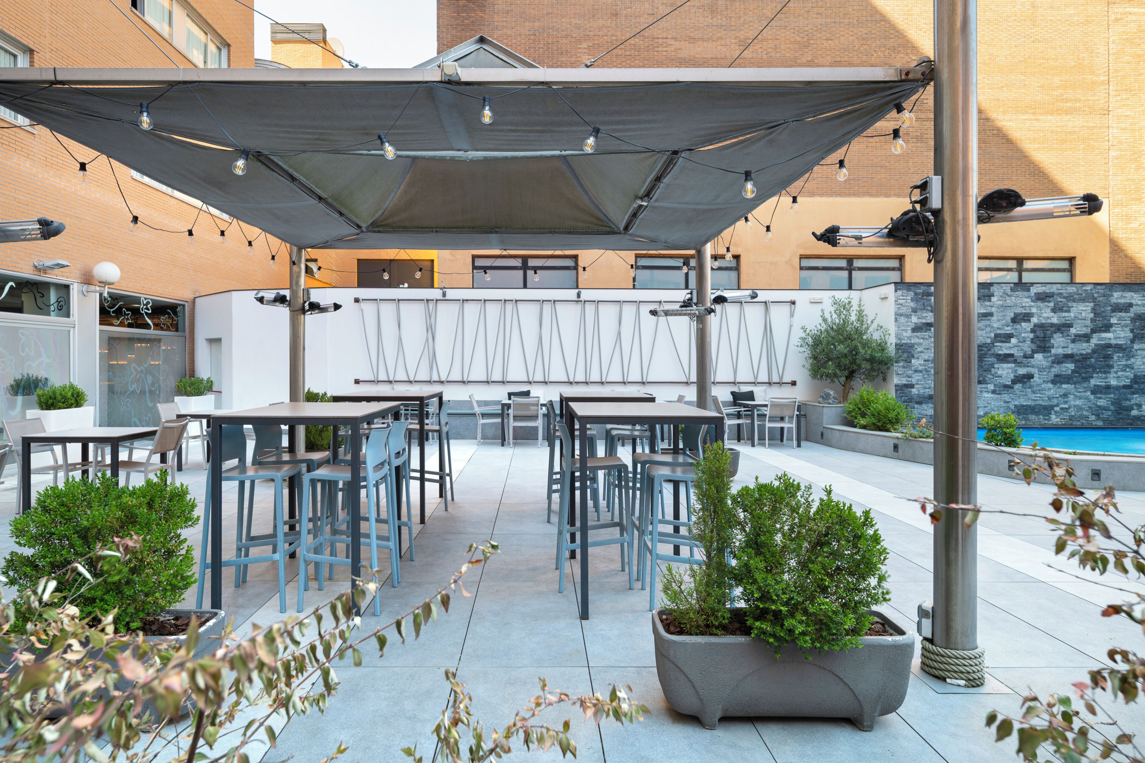 An outdoor patio area with tables and chairs, a pool, and a covered seating area.