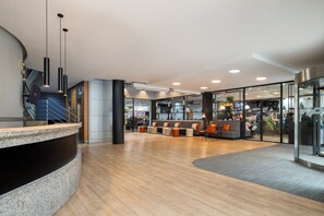 A modern lobby with a curved reception desk, seating area, and glass doors leading to a dining space. -  Dorma Juan de Austria (Valladolid)