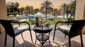 A balcony with a view of a swimming pool, palm trees, and lounge chairs. - Metropolitan Al Mafraq Hotel (Abu Dhabi)