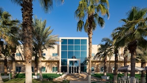 A modern building with a glass facade, surrounded by palm trees and a well-maintained lawn. - Metropolitan Al Mafraq Hotel (Abu Dhabi)