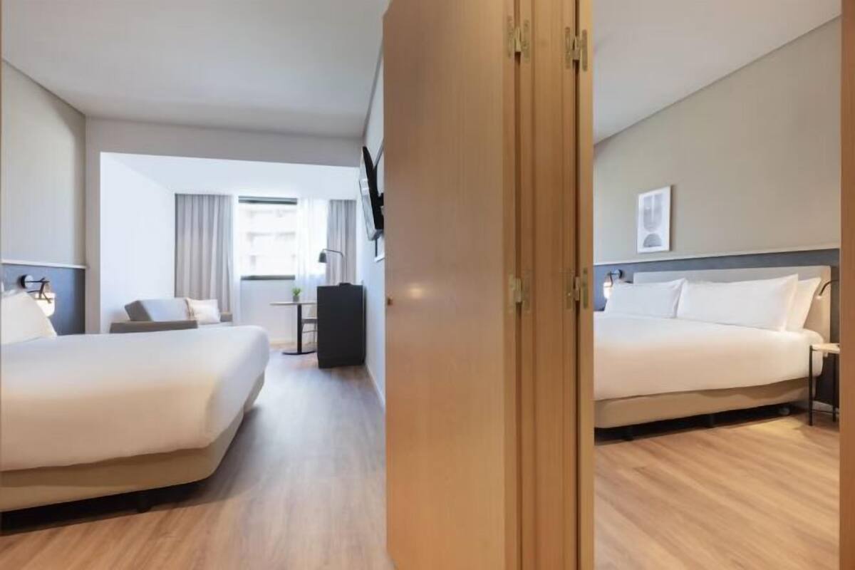 Habitación de hotel con dos camas, un escritorio, una silla, un televisor y una ventana con cortinas.