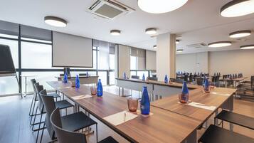 A conference room with long tables, chairs, and a projector screen.