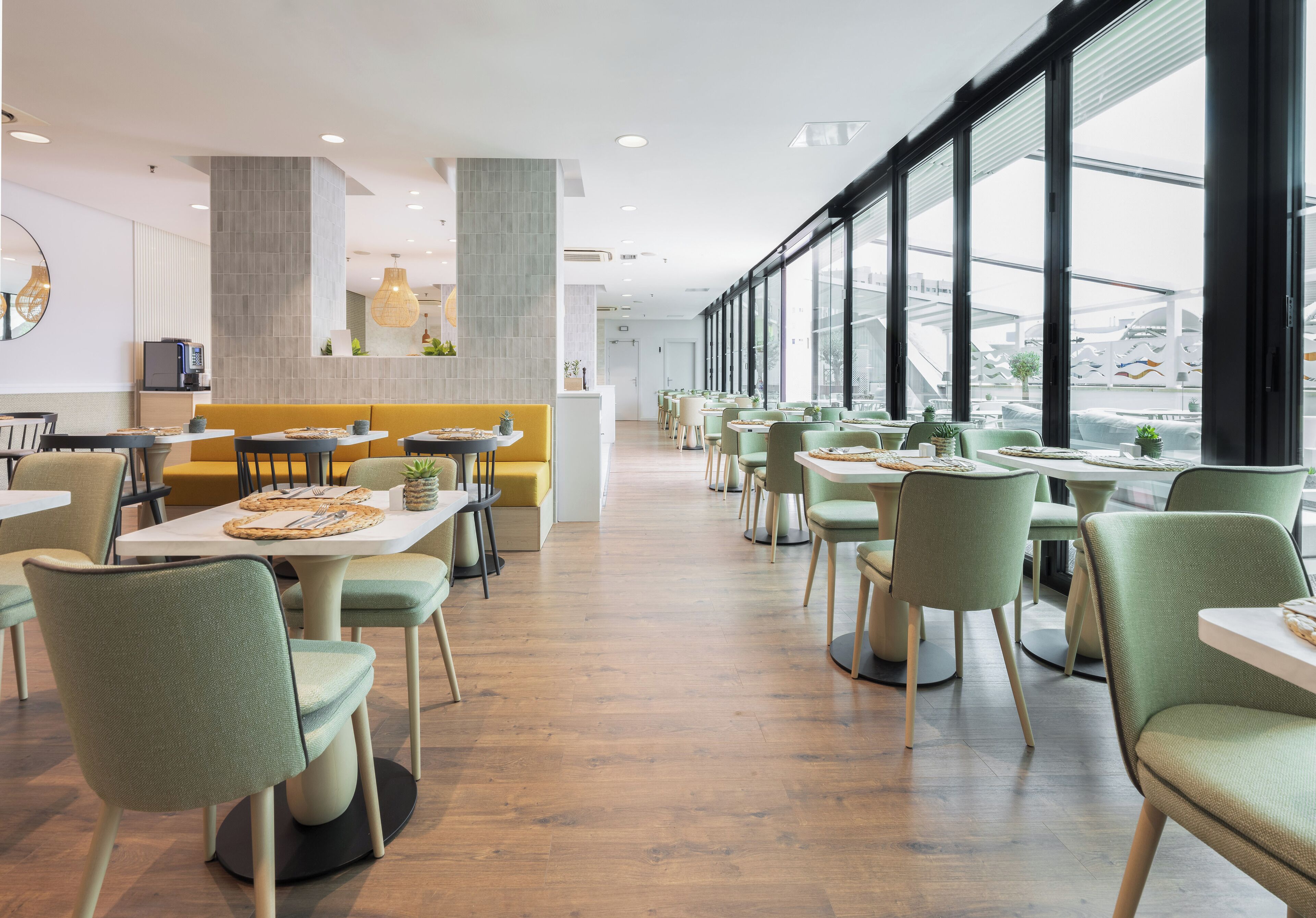 Un espace de restauration moderne avec des tables et des chaises hautes, un coin salon central et de grandes fenêtres offrant une vue dégagée.