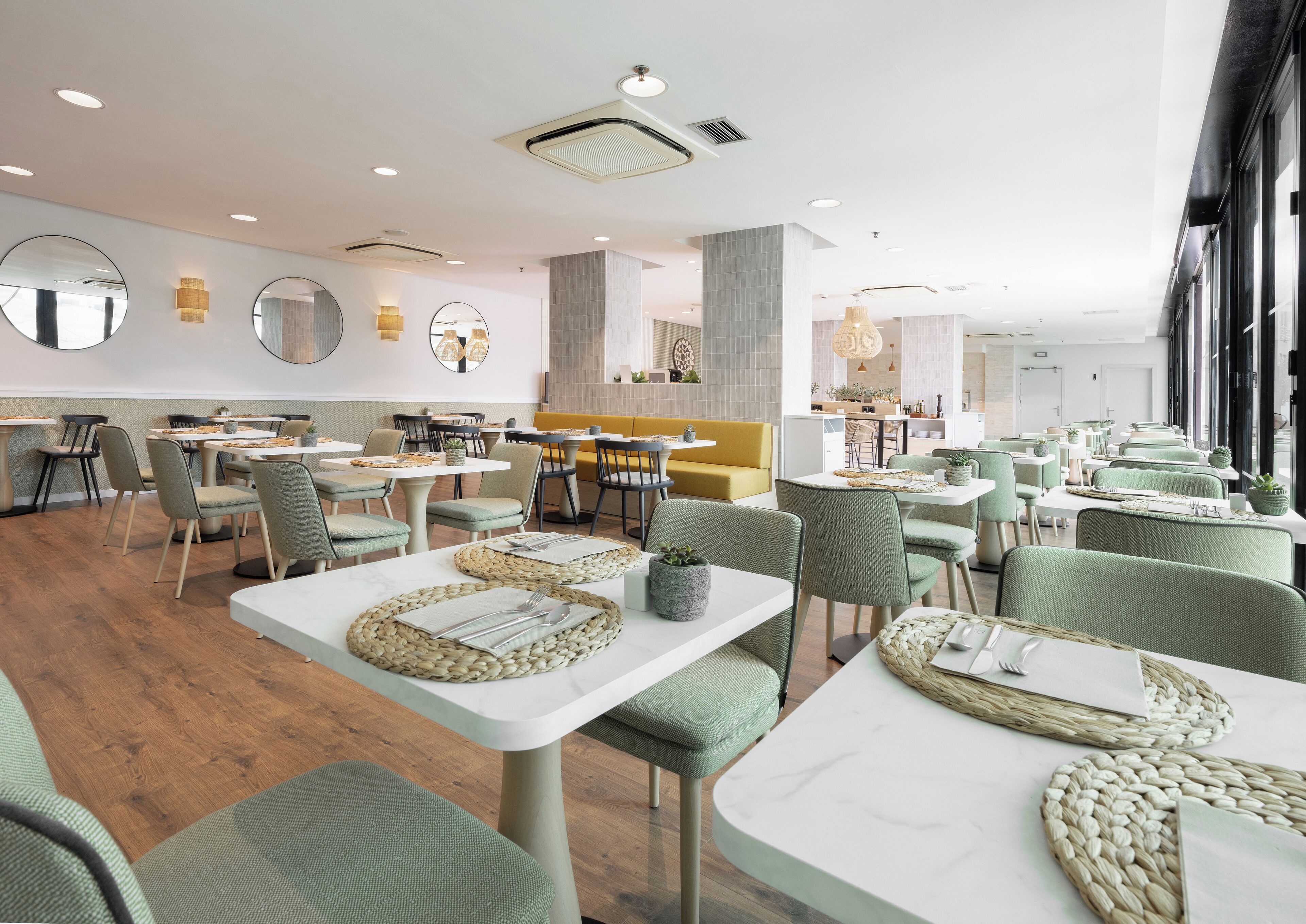 Ein modernes Restaurant mit runden Tischen, grünen Stühlen und einem gelben Sofa.
