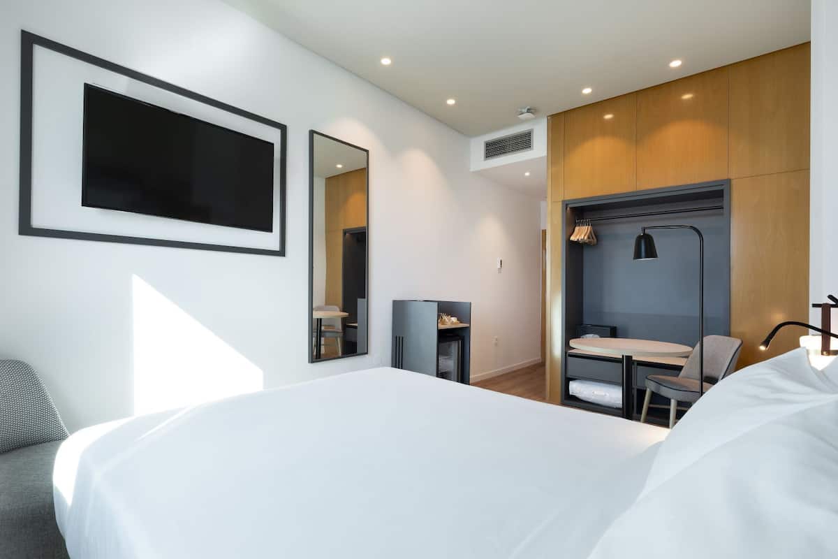 Moderni hotellihuone, jossa on suuri sänky, työpöytä tuolilla, peili ja vaatekaappi.