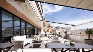 Une terrasse sur le toit, dotée d’un espace extérieur aménagé avec des sièges, de grandes fenêtres et des plantes en pot.